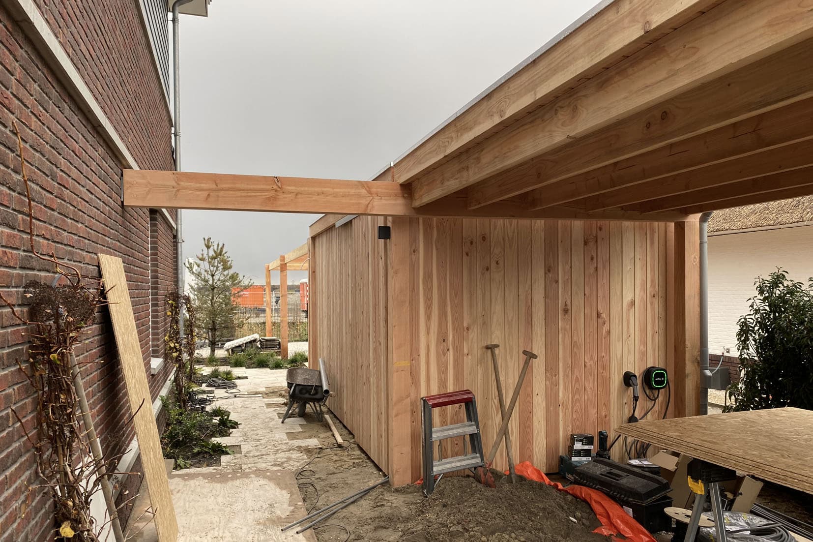 De lange constructie van douglashout verbindt carport, sauna en buitenkeuken.